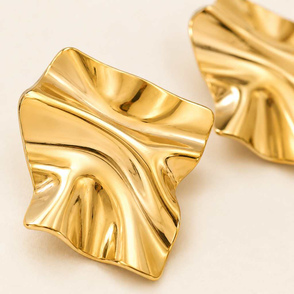A pair of gold-toned, wavy, leaf-shaped earrings with a polished metallic finish.