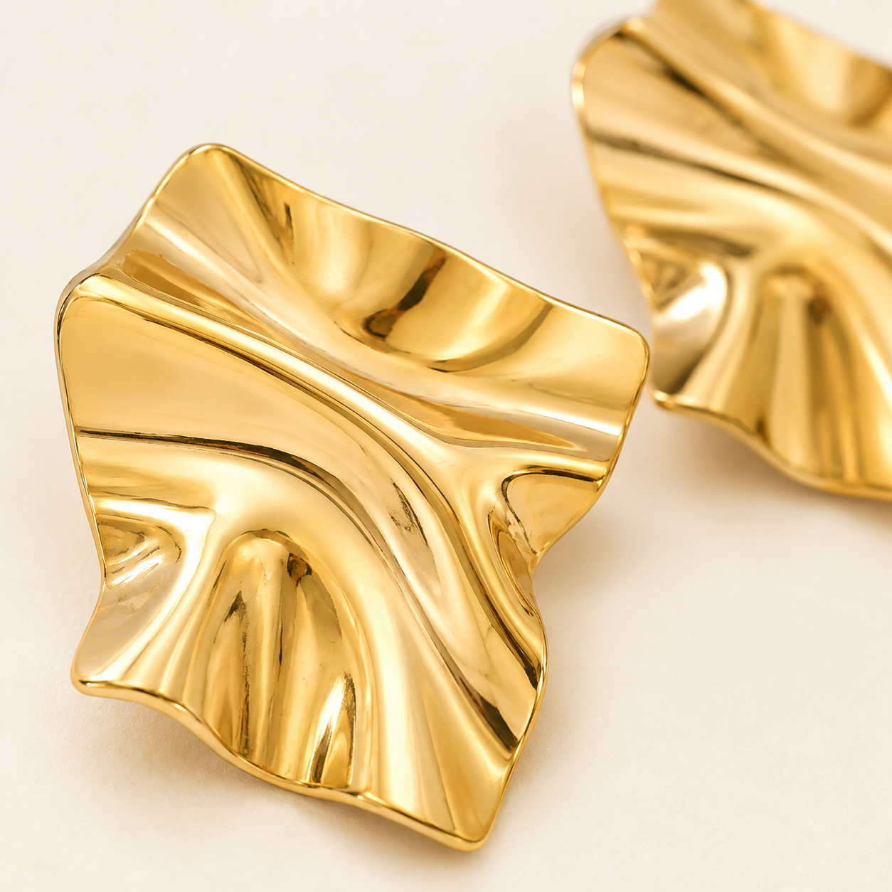 A pair of gold-toned, wavy, leaf-shaped earrings with a polished metallic finish.