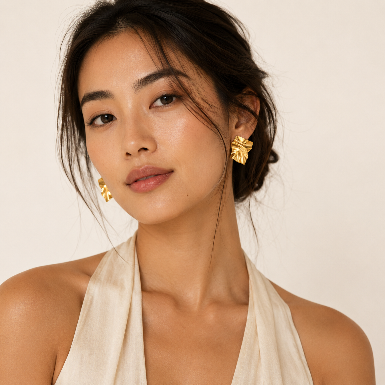 A close-up of a woman wearing textured gold geometric earrings.