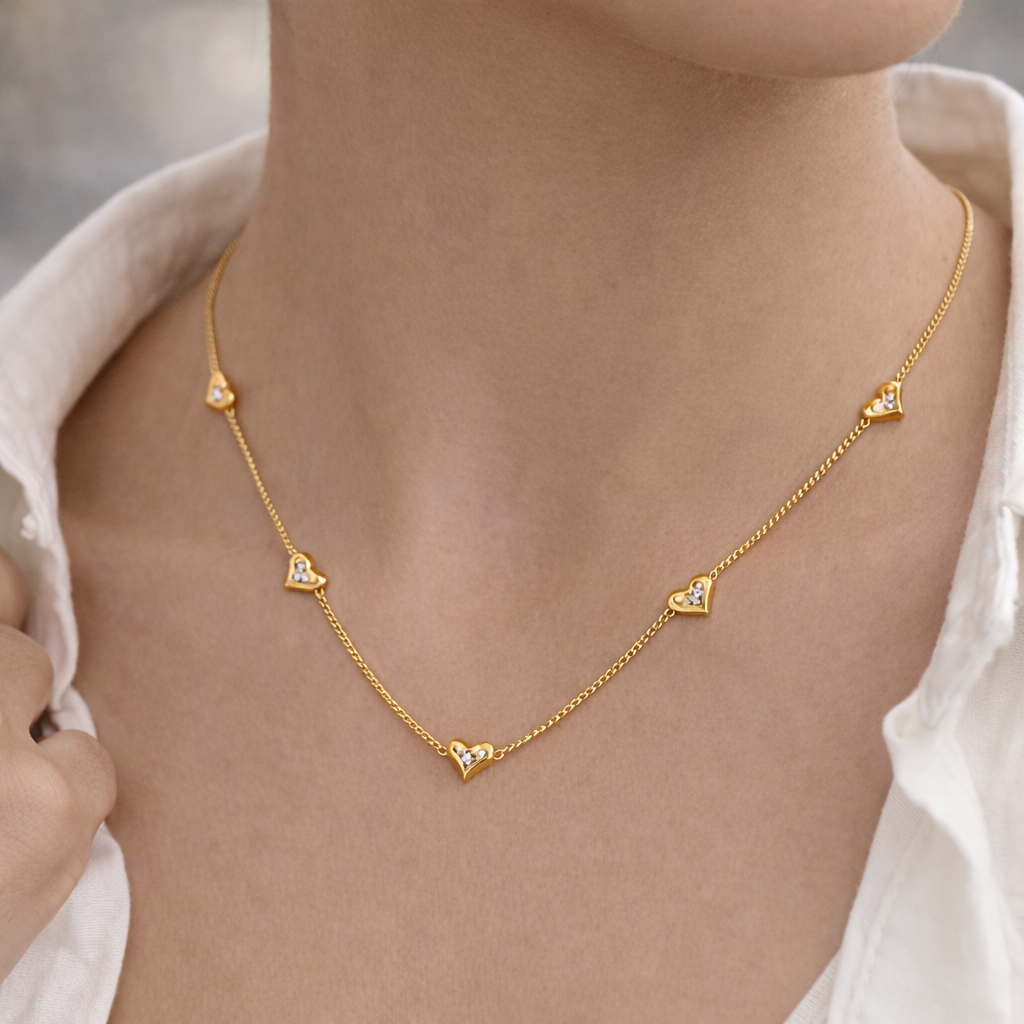 Gold necklace with heart-shaped pendants on a person wearing a white shirt.