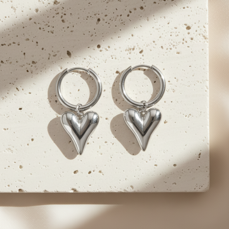 Silver heart-shaped earrings on a textured beige surface