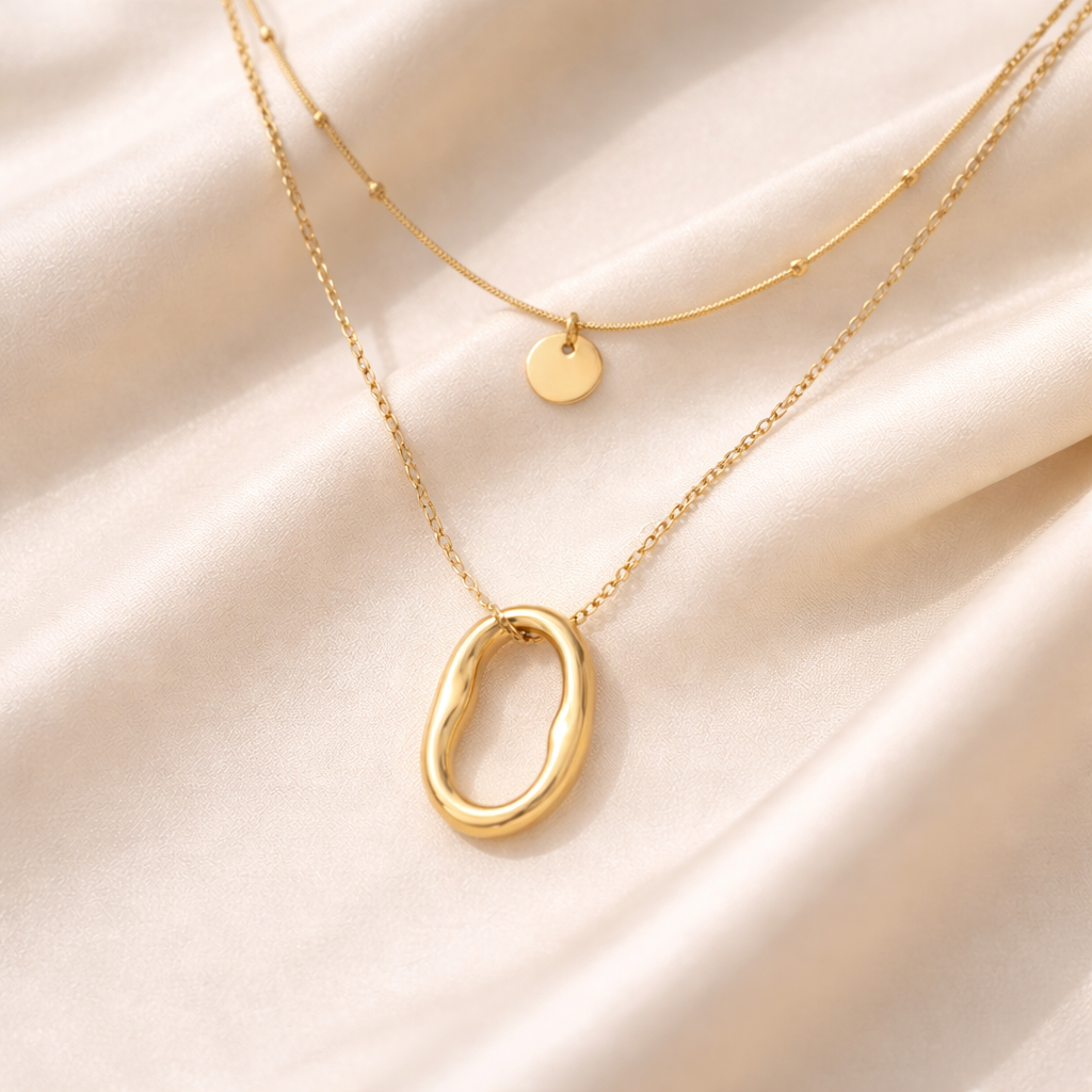 Close-up of oval pendant layered gold necklace on silky background