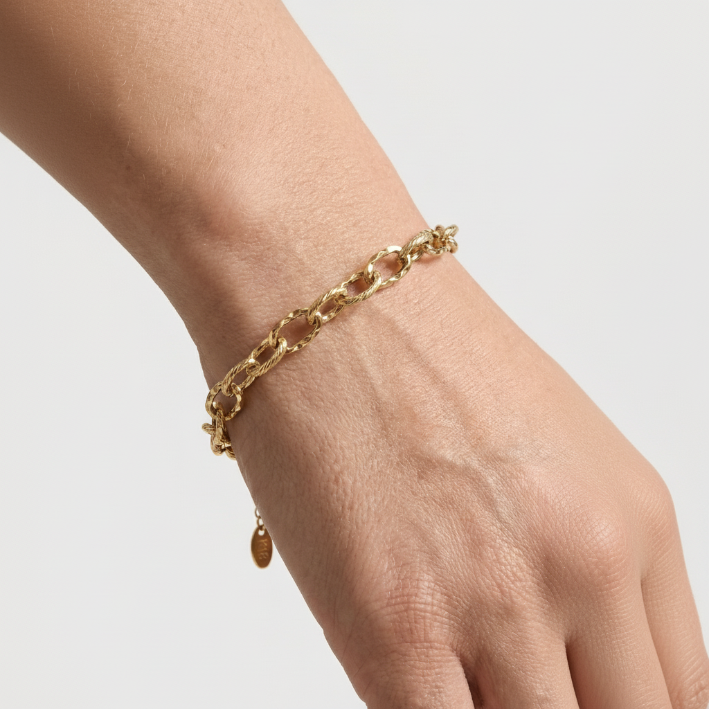 Gold chain bracelet on a wrist against a light gray background